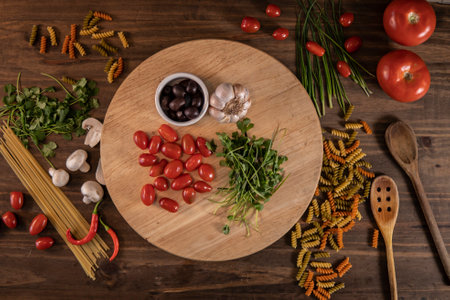Flat lay of vegetables and pasta and a chopping board over a wooden tableの写真素材