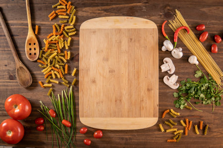Flat lay of vegetables and pasta and a chopping table over a wooden tableの写真素材