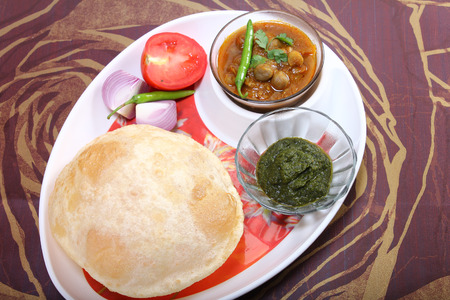 plate of spicy chole bhature, with green chili topping and chutneyindian dish