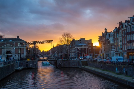 The sun setting behind buildings overlooking a canal in Amsterdamのeditorial素材