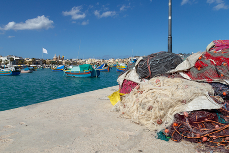 Fishing nets stand on a concrete jetty in Marsaxlokk, Malta. Typical luzzu fishing boats can be seen in the backgroundのeditorial素材