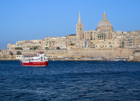 A red and white boat full or tourists, enters Marsamxett harbor for a sightseeing cruise on a bright clear dayのeditorial素材