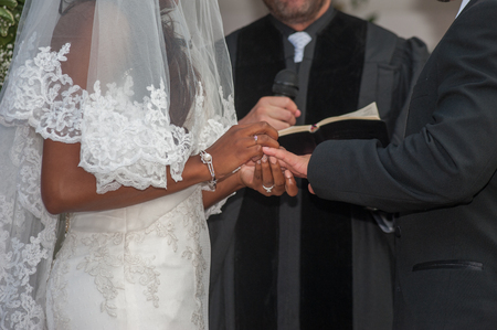 Bride places ring on groom's finger at alter.の写真素材