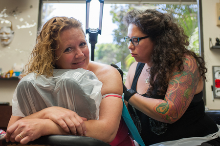 Middle age female with forced smile receiving a tattoo.の写真素材