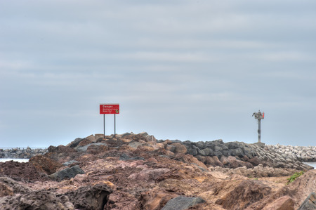Danger sign on top of the jetty rocks.の写真素材