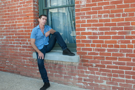 Male model seated in window of red brick wall.の写真素材