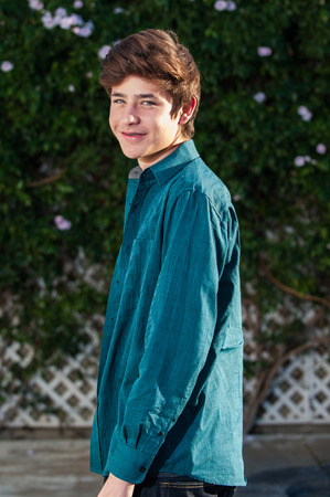 Upper body of handsome Latino teen smiling while turned at waist.
