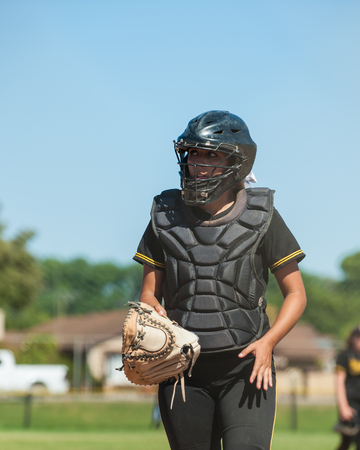 Softball catcher in black uniform with glove off of hand.