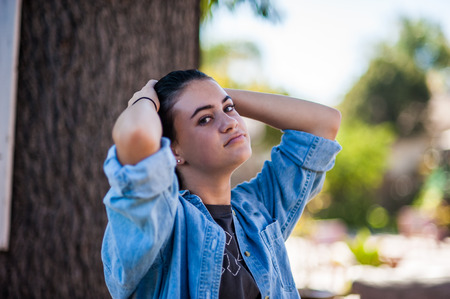 Female teen running hands through hair under shade of a tree in garden.の写真素材