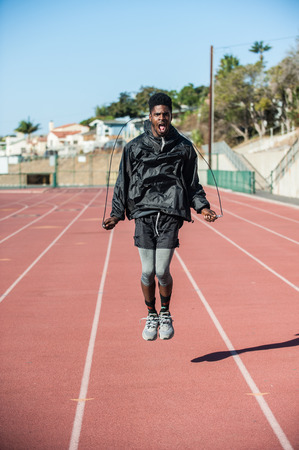 Lean Jamaican athlete jumping rope with intense look on face on track at stadium.