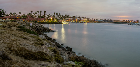 Panoramic scene of calm marina waters reflecting the night lights and lamps off the surface in the...