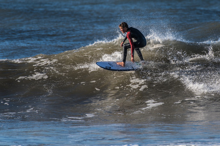 Young male surfer taking high line near wave lip while surfing remaining northwest swell in Ventura,...