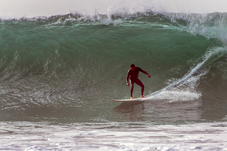 Goofy foot surfer in black wetsuit dropping into barrel of very large set waves from winter swell in...