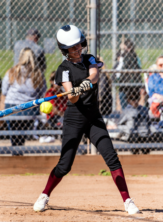 Female softball player in black uniform making contact with bat on pitched ball during game.の写真素材