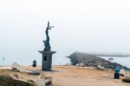 Ventura statue greets boats of passage as fog shrouds the view across the end of harbor mouth jetty.の写真素材