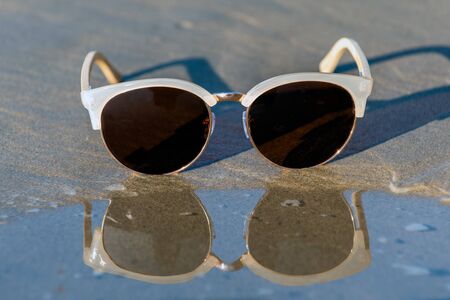Contemporary sunglasses fashion shows aviator style dark tinted lenses reflected on wet shoreline of sunny beach.の写真素材