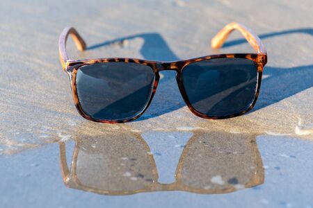 Contemporary sunglasses fashion shows leopard print style dark tinted reflective lenses reflected on wet shoreline of sunny beach.の写真素材