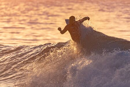 Surfer contestant in contest jersey is silhouetted against the reflective ocean water during golden...