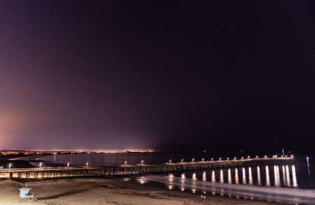 Pier lamps reflect in the ocean water under the Ventura Pier with constellation stars in sky above.の写真素材