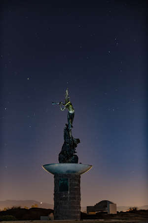 Mermaid statue stands lit against the night sky full of stars and constellations in Autumn night.の素材 [FY310158078978]