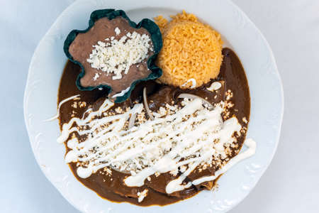 Overhead view of enchiladas mole served with rice and tortilla chip bowl refried beans looks and tastes appealing.の写真素材