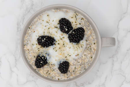 Black berries and hemp seed on top of oatmeal ready to eat in a bowl on the table is a great way to start the day with a good source of fiber and protein.の写真素材