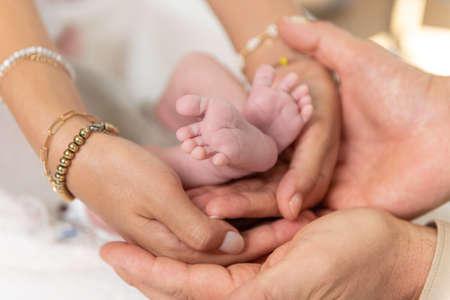 Tiny newborn baby feet cradled by mother and father hands in a show of family togethernessの写真素材