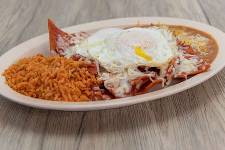 Chilaquiles, covered in fried eggs and served on a plate with rice, and beans for a very hearty Mexican meal.の写真素材