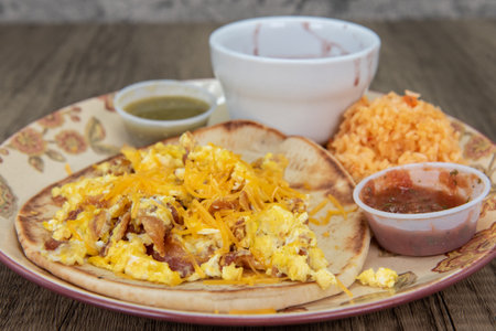 Thick homemade tortilla holds a breakfast taco covered with melted cheese, cilantro and salsa dipping sauce for a fullfilling meal.の写真素材