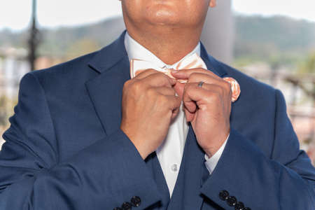 Groom adjusting his bow tie on the big day of his wedding.の写真素材