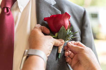 Hands helping pin the boutonniere onto the lapel of his suit jacket by pushing with the thumbs.の写真素材