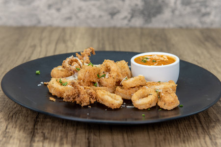 Tempting appetizer of breaded calamari rings with dipping sauce and served on a small plate.