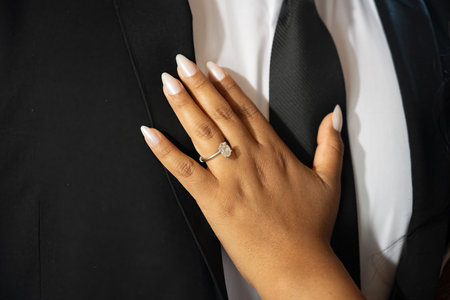 Bride to be hand and fingers show the engagement diamond ring resting on boyfriends suit and tie.の写真素材