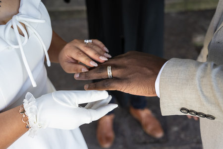 Newly married bride places wedding ring on the black finger of her husband hand during ceremony.の写真素材