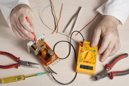 Hand of electrician with multimeter probe at  electrical switchgear cabinet.