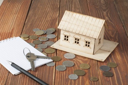 Home savings, budget concept. Model house, notepade, pen, calculator and coins on wooden office desk tableの写真素材