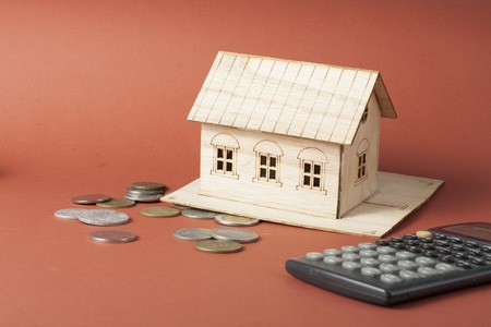 Home savings, budget concept. Model house, notepade, pen, calculator and coins on wooden office desk tableの写真素材