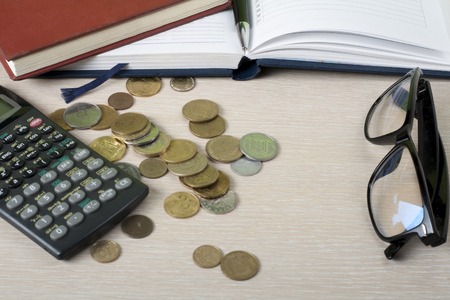 Home savings, budget concept. Notepad, calculator, eyeglasses and coins on wooden office desk table.の写真素材