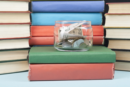 Money in glass jar and stack of books on wooden table.Saving, financial and education concept.の写真素材