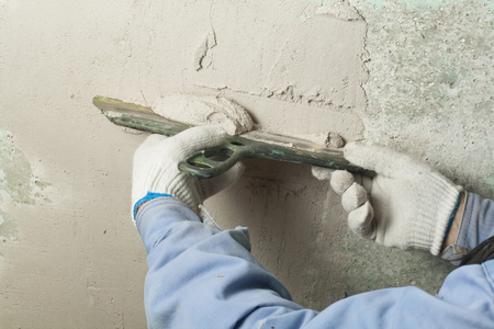 Construction and renovation concept. Hand of man in glove with trowel during repair of wall.の写真素材