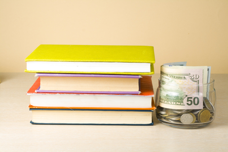 Money in glass jar and stack of books on wooden table.Saving, financiai and education concept.の写真素材