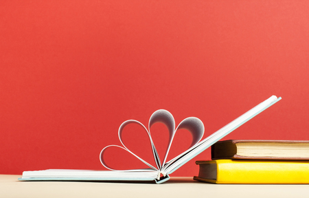 Opened book with pages in shape of heart. Red background. Free copy space .の写真素材