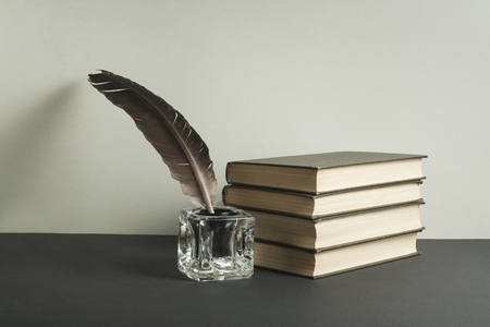 Stack of books and quill pen with inkwell on wooden table. Free copy space.の写真素材