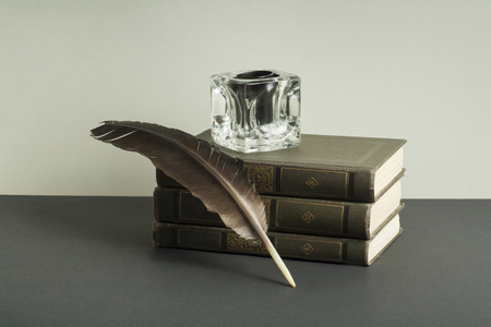 Stack of books and quill pen with inkwell on wooden table. Free copy space.の写真素材
