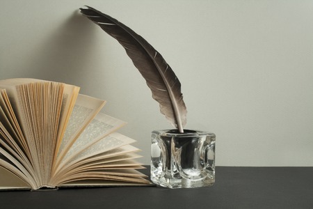 Open book and quill pen with inkwell on wooden table. Free copy space.の写真素材