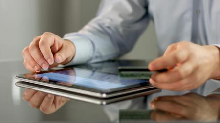 Male hands making online noncash payment on tablet, inserting bank card detailsの写真素材