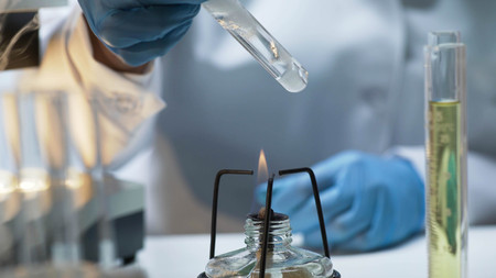 Scientist holding tube with boiling fuming liquid over burner, lab experimentの写真素材