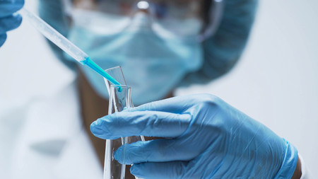 Female chemist adds drops of blue substance into test tubes, lab researchの写真素材