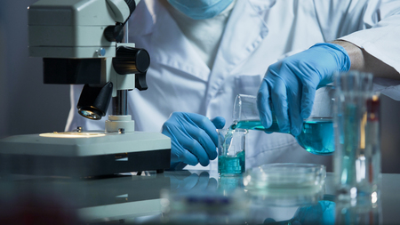 Lab assistant pouring liquid reagent into beaker to create chemical solution