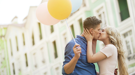 Happy couple with colorful air balloons kissing in street, tender relationshipの写真素材